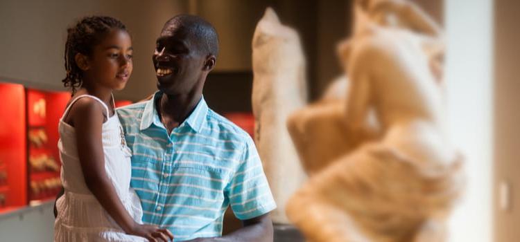 a father 和 his daughter smile 和 look at sculptures in an art museum